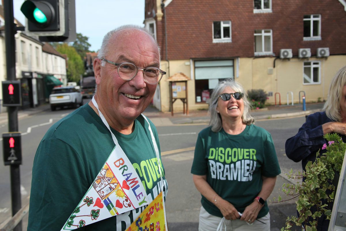 Five smiling volunteers in green Discover Bramley t-shirts standing together under a gazebo branded with discoverbramley.co.uk and bunting flags
