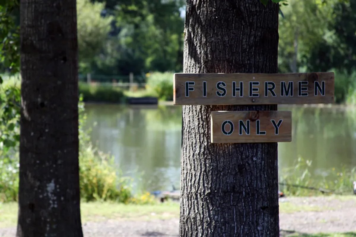 A wooden sign nailed to a tree in front of a lake that says Fishermen only