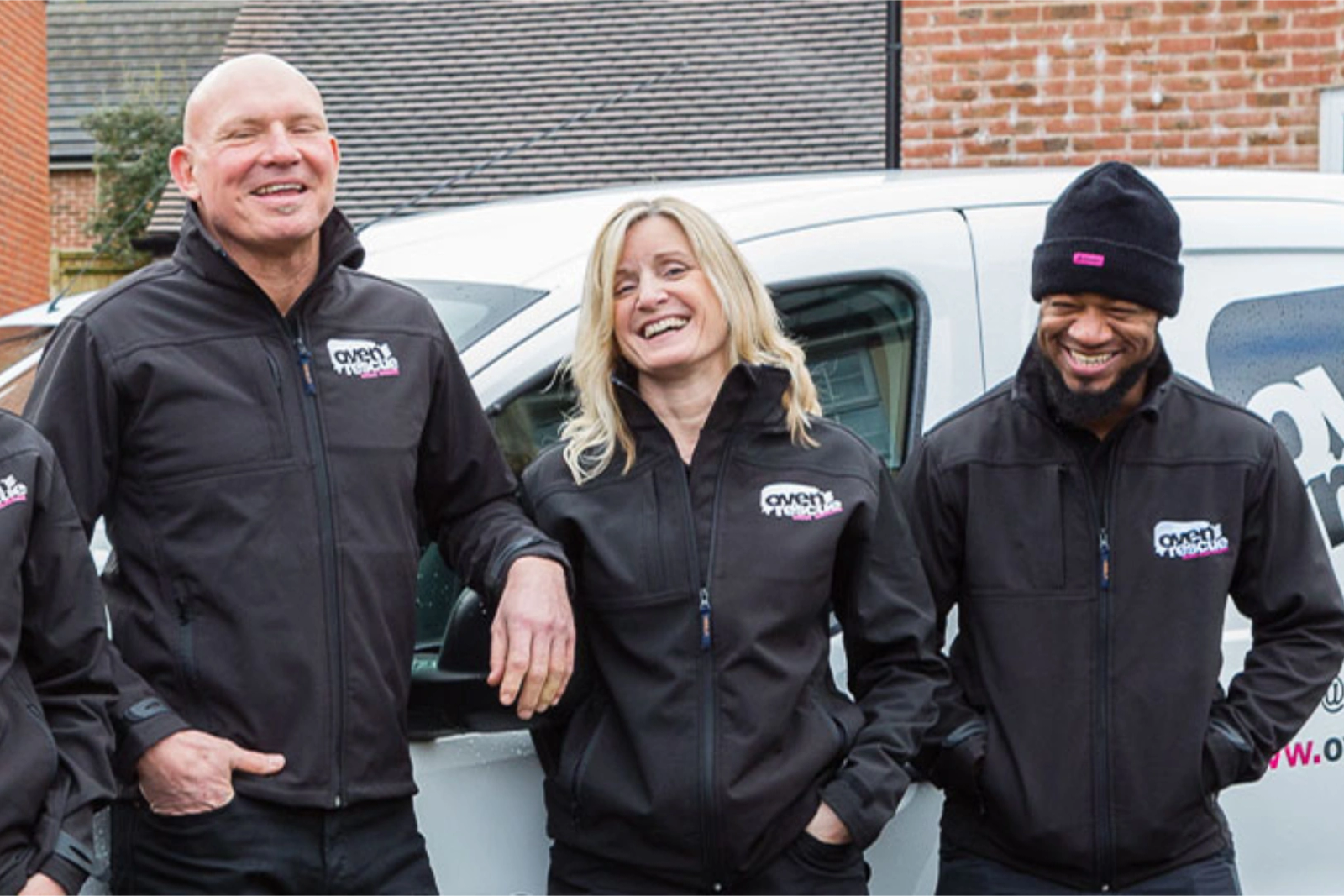 Three Oven Rescue team members in branded jackets laughing together in front of a company van