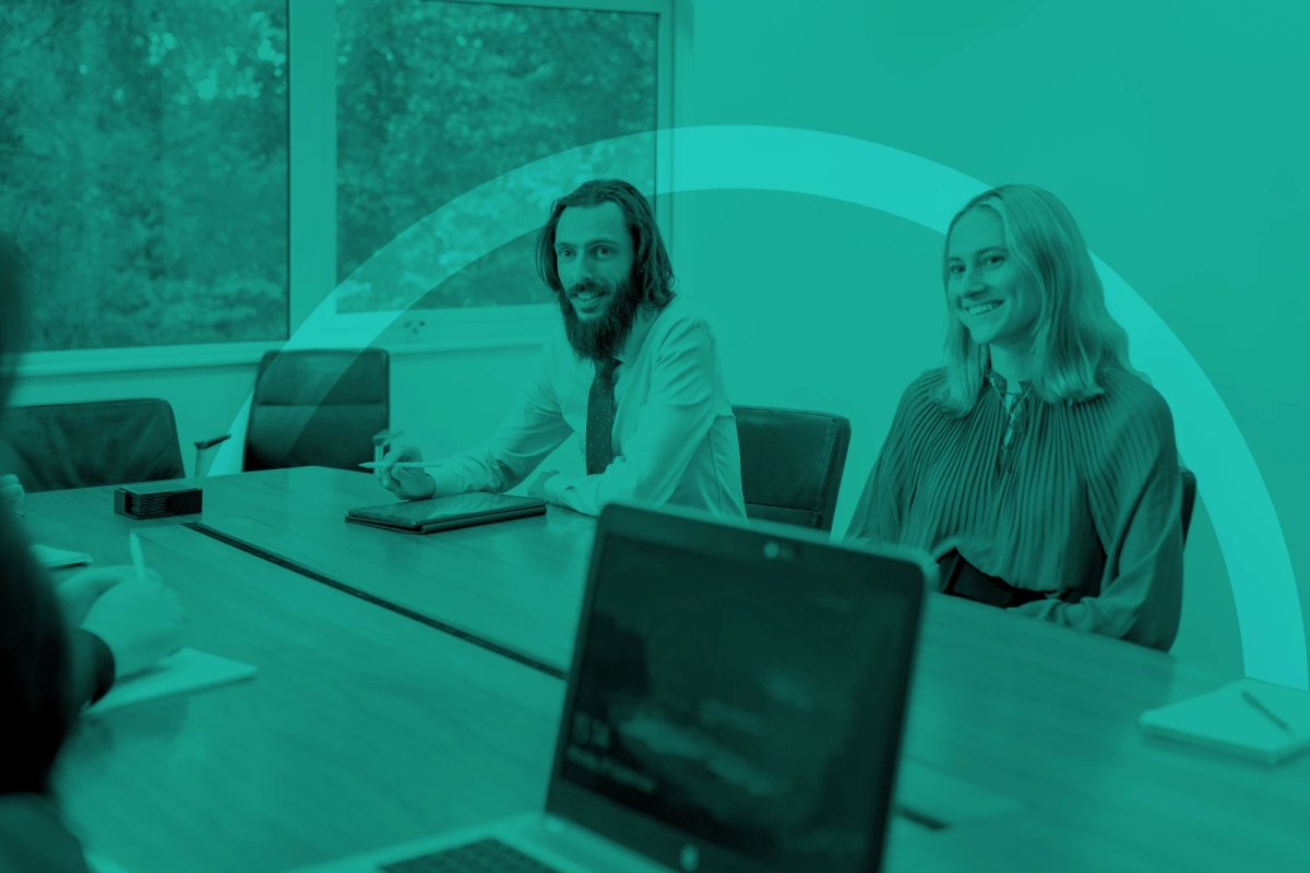Two Bessler Hendrie staff members sitting at a boardroom table during a meeting, shown in a teal duotone treatment