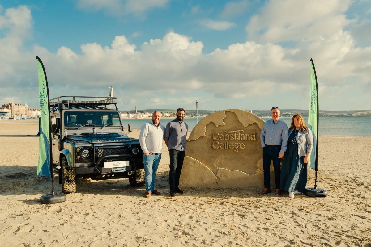 A sand sculpture engraved with the Coastland College name, with a branded Land Rover Defender on the beach