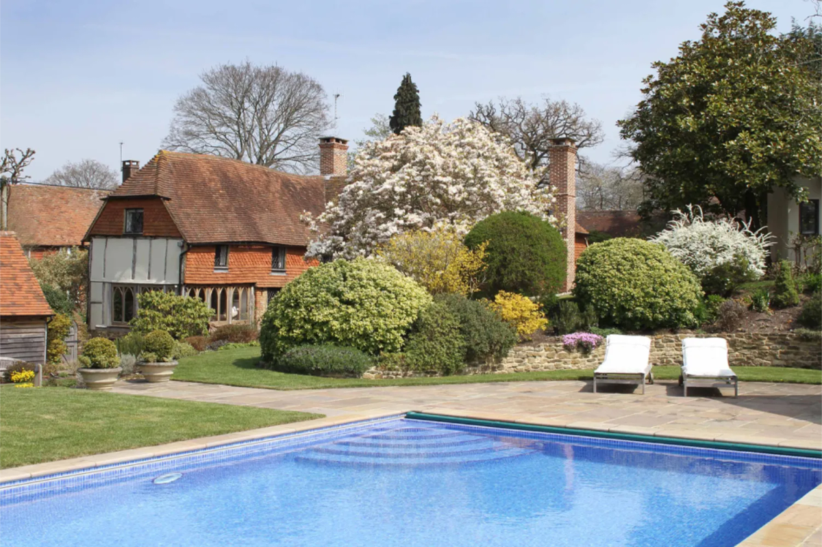 Outdoor swimming pool in front of a traditional Surrey country house surrounded by mature gardens