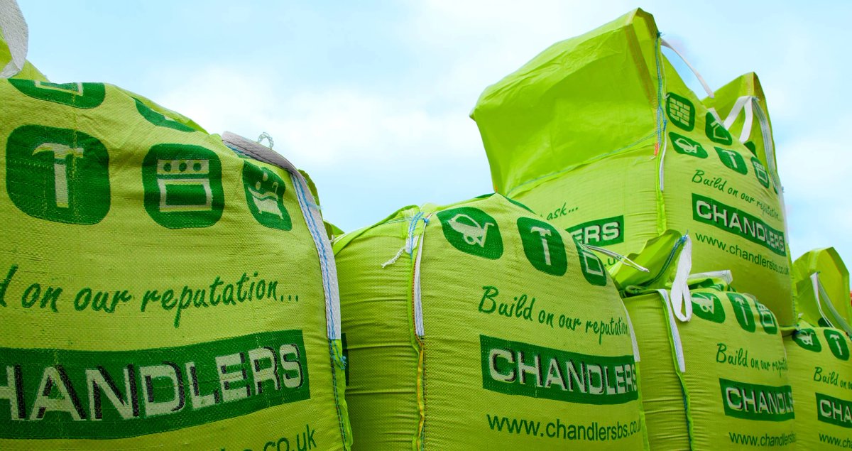 Stacked bright green Chandlers branded builders' bags printed with category icons and the 'Build on our reputation' tagline