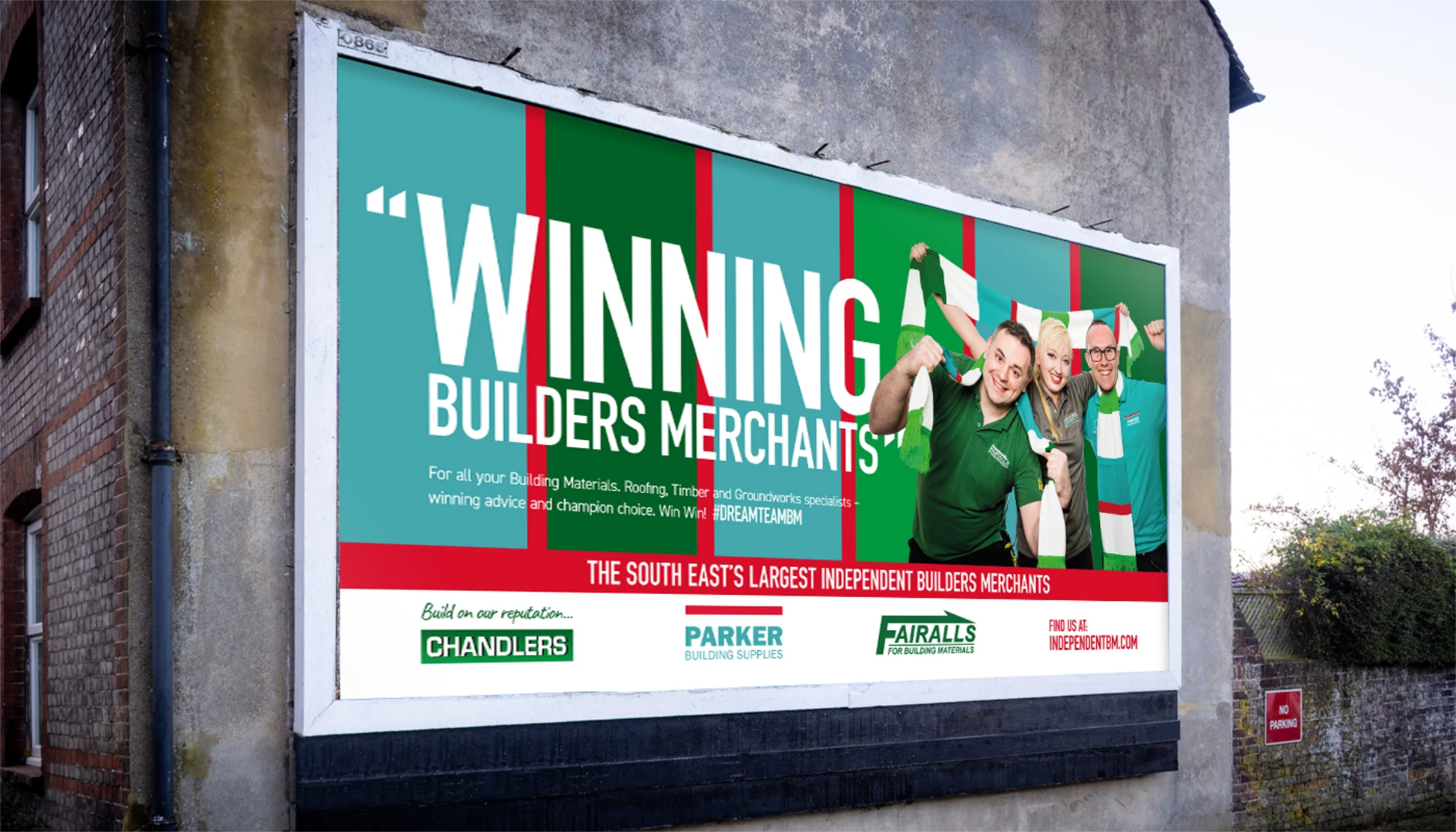 A billboard reading 'Winning Builders Merchants' with three staff members holding up green and white scarves, mounted on the side of a building