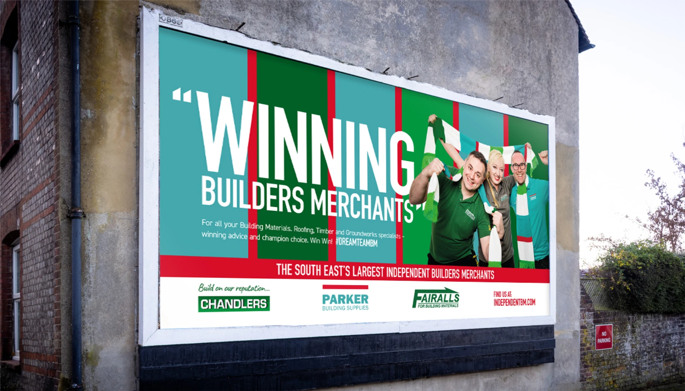 A billboard reading 'Winning Builders Merchants' with three staff members holding up green and white scarves, mounted on the side of a building
