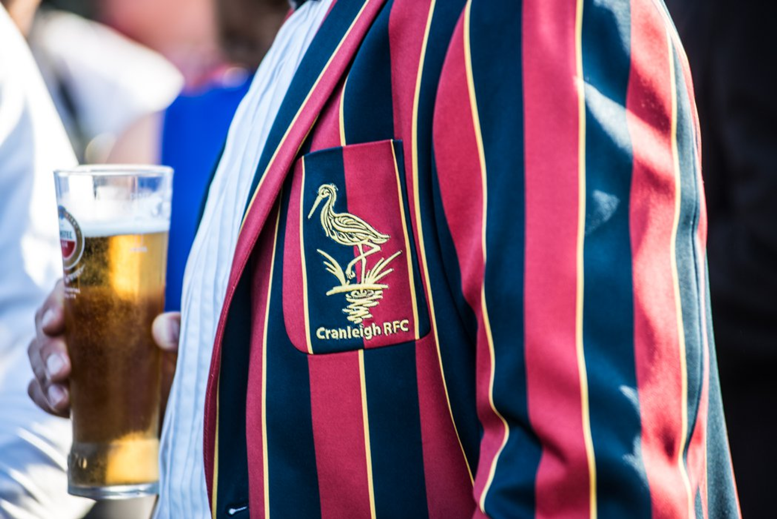 A man in a striped Cranleigh RFC blazer holding a pint of beer