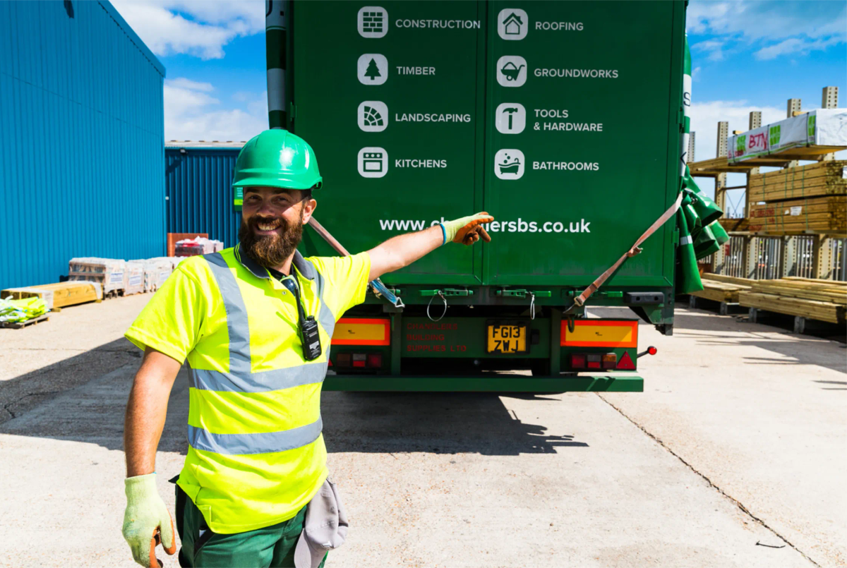 A smiling Chandlers driver in a hi-vis vest and hard hat pointing to the website address on the back of a branded delivery lorry