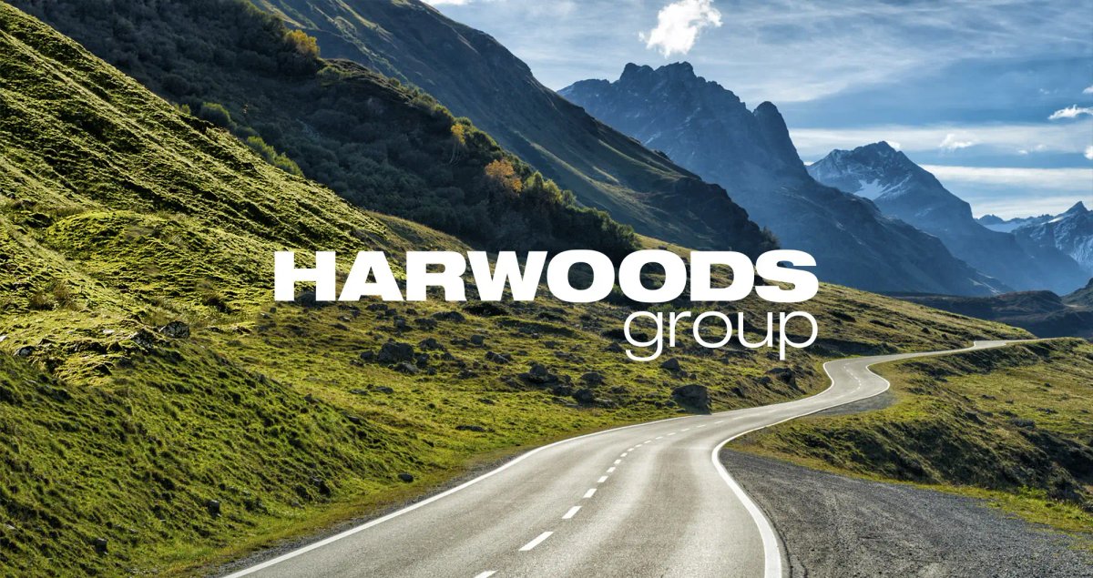 Winding mountain road through green hills with the Harwoods Group logo overlaid