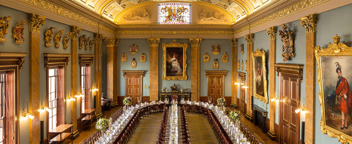 The ornately decorated banqueting hall of Fishmongers' Hall, with gilded columns, portraits, coats of arms and a long table set for a formal dinner