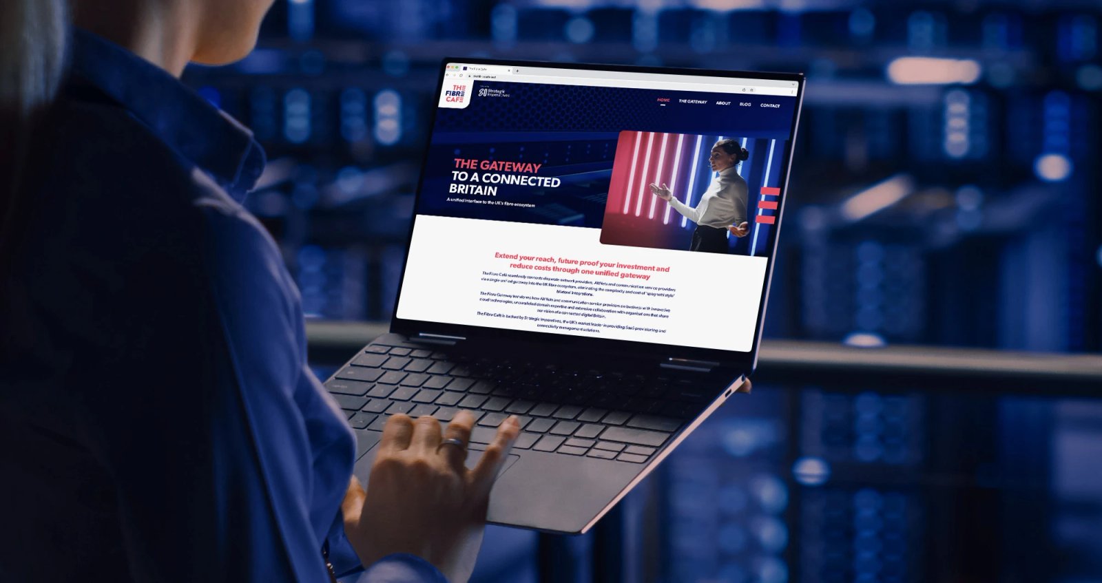 A person holding a laptop displaying The Fibre Café website homepage with the headline 'The Gateway to a Connected Britain'