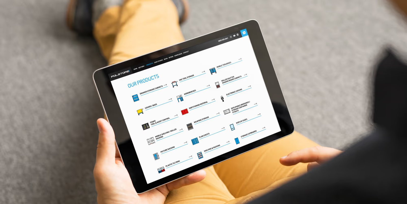 A person holding a tablet displaying the Polstore website 'Our Products' page, with a full list of storage solutions