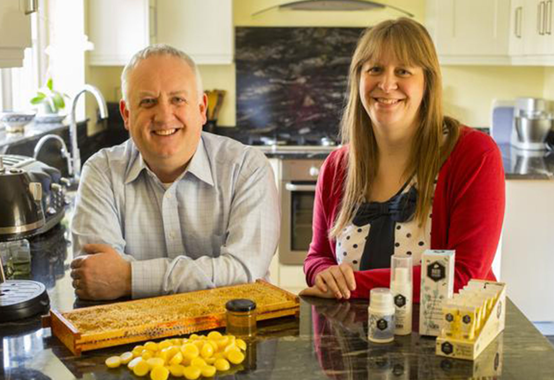 An image of the founders of Bee Good Cosmetics in their kitchen, with an arrangement of products in front of them