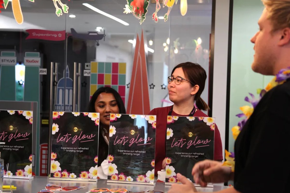 People standing around some laid out laminated ads for Solait that say "Let's glow" in a neon effect typography.