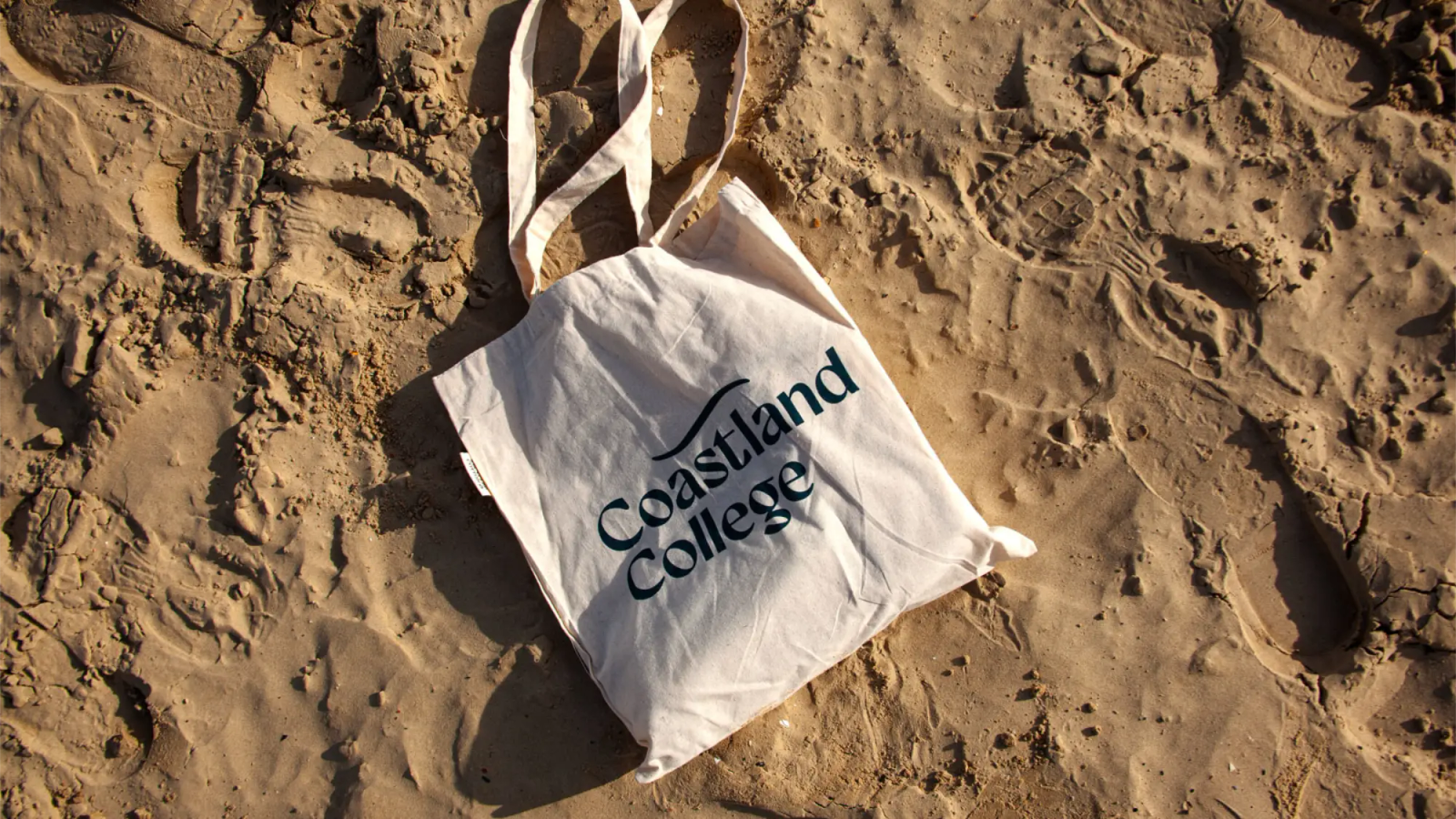 A tote bag on the sand that says Coastland College