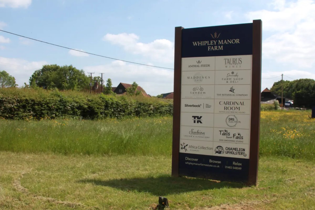 A tall vertical Whipley Manor Farm directory sign listing on-site businesses such as Maddings Cafe, Taurus Wines and the farm shop.