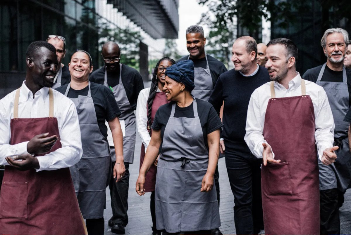 A group of kitchen and front-of-house staff in aprons walking together and laughing outdoors