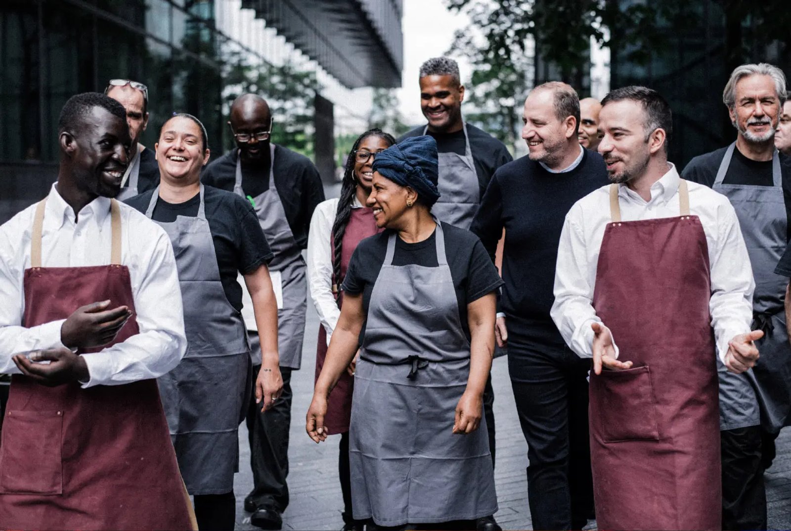 A group of kitchen and front-of-house staff in aprons walking together and laughing outdoors