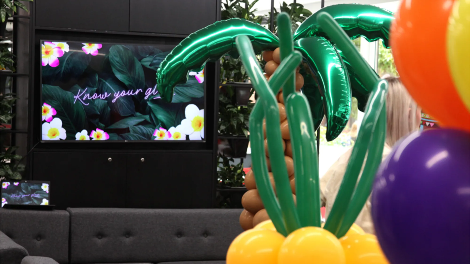 Presentation room with inflatable tropical plants with a tv in the background showing the Solait branding animation.