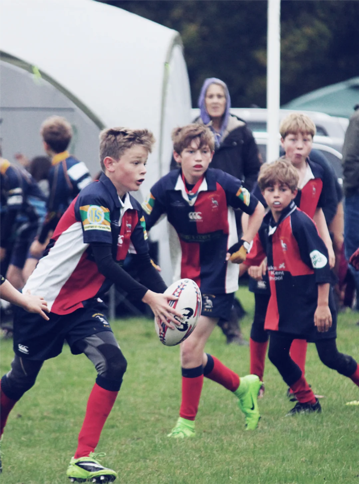 A group of junior rugby players in red, white, and navy kit running with the ball during a match