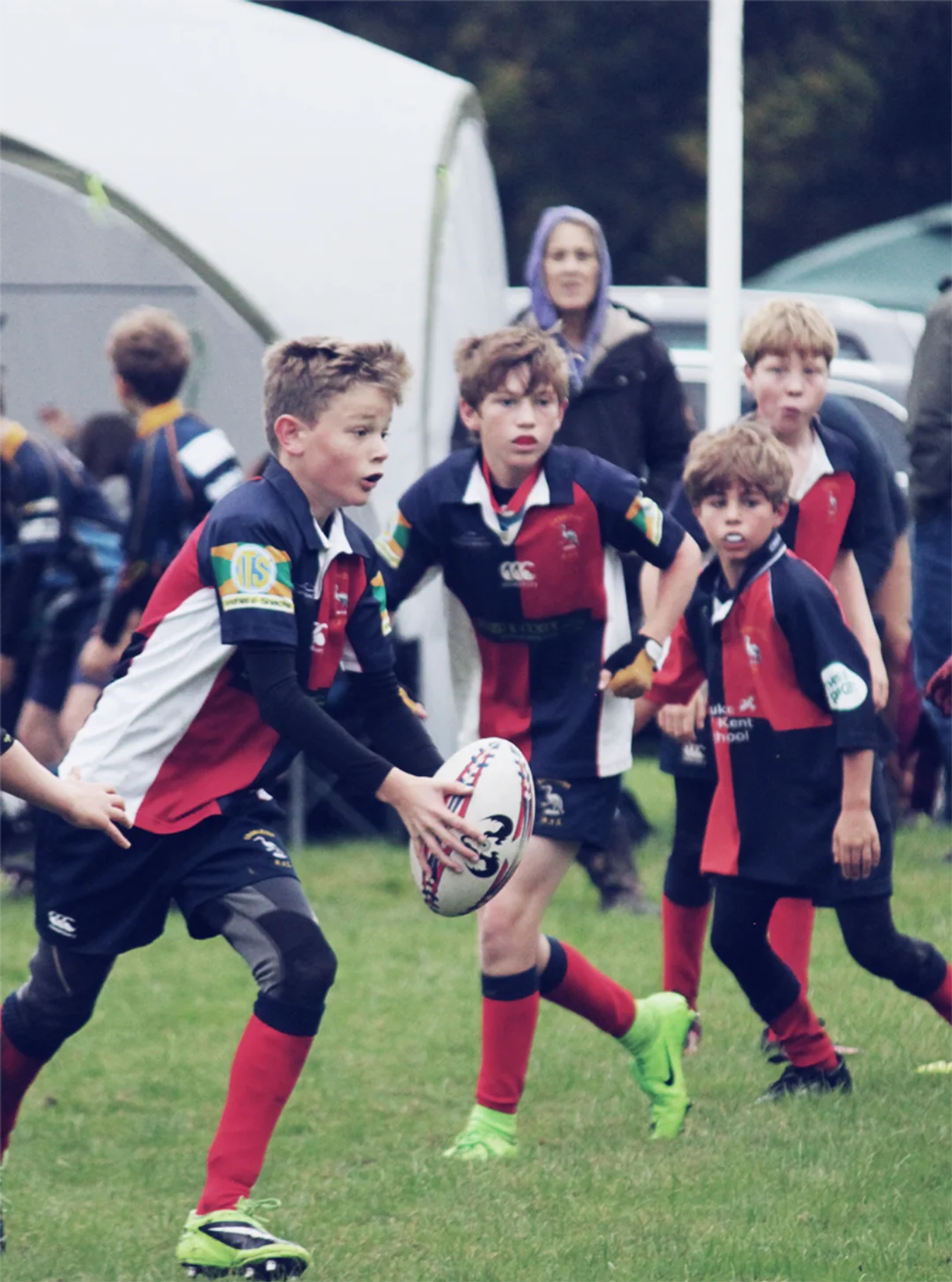 A group of junior rugby players in red, white, and navy kit running with the ball during a match