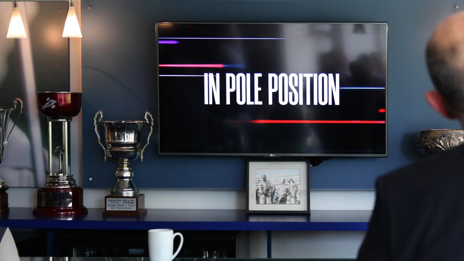 Wall-mounted TV displaying the "In Pole Position" animation above a shelf of racing trophies