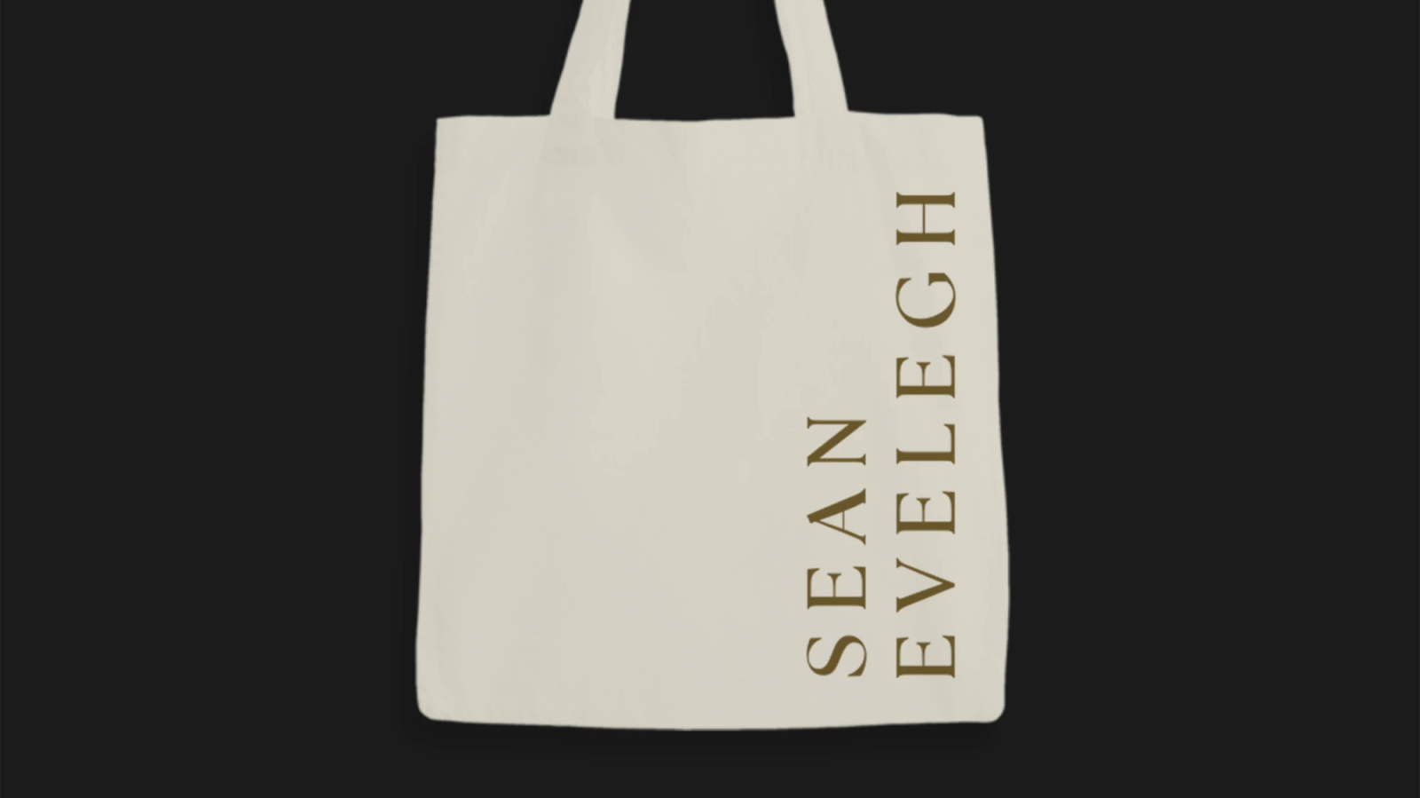 A cream tote bag with the Sean Evelegh wordmark printed in gold