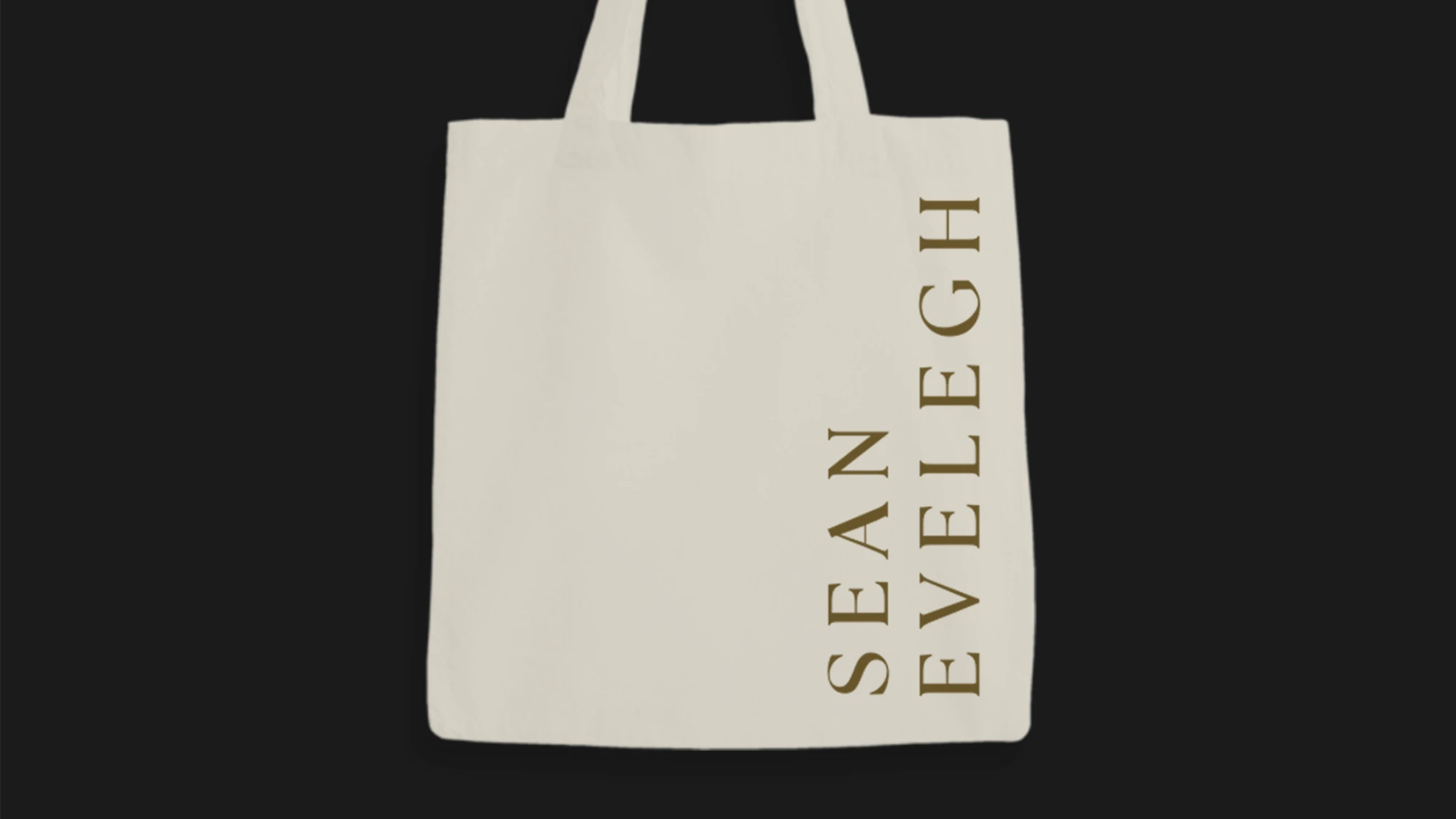 A cream tote bag with the Sean Evelegh wordmark printed in gold