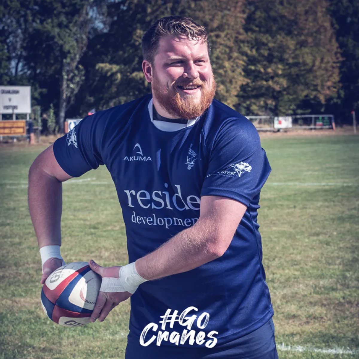 A Cranleigh RFC player in a navy sponsored jersey holding a rugby ball on the pitch, with '#GoCranes' text overlay
