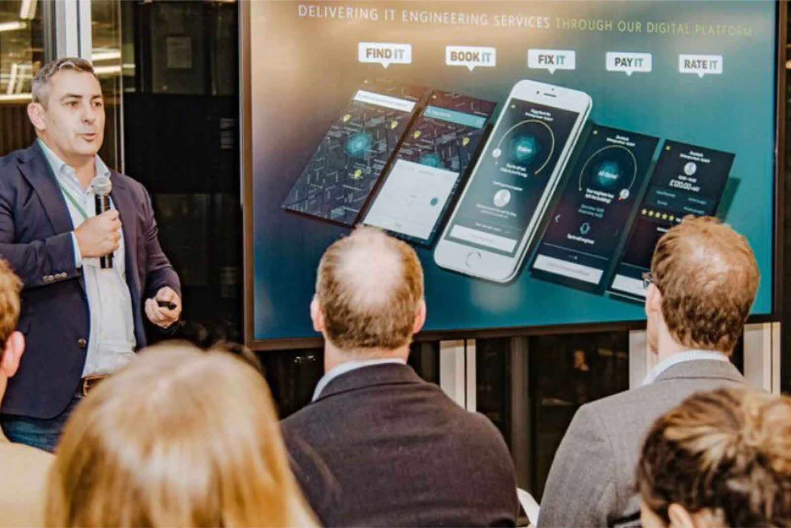 Brett holding a microphone giving a speech with a branded Itarmi slide in the background