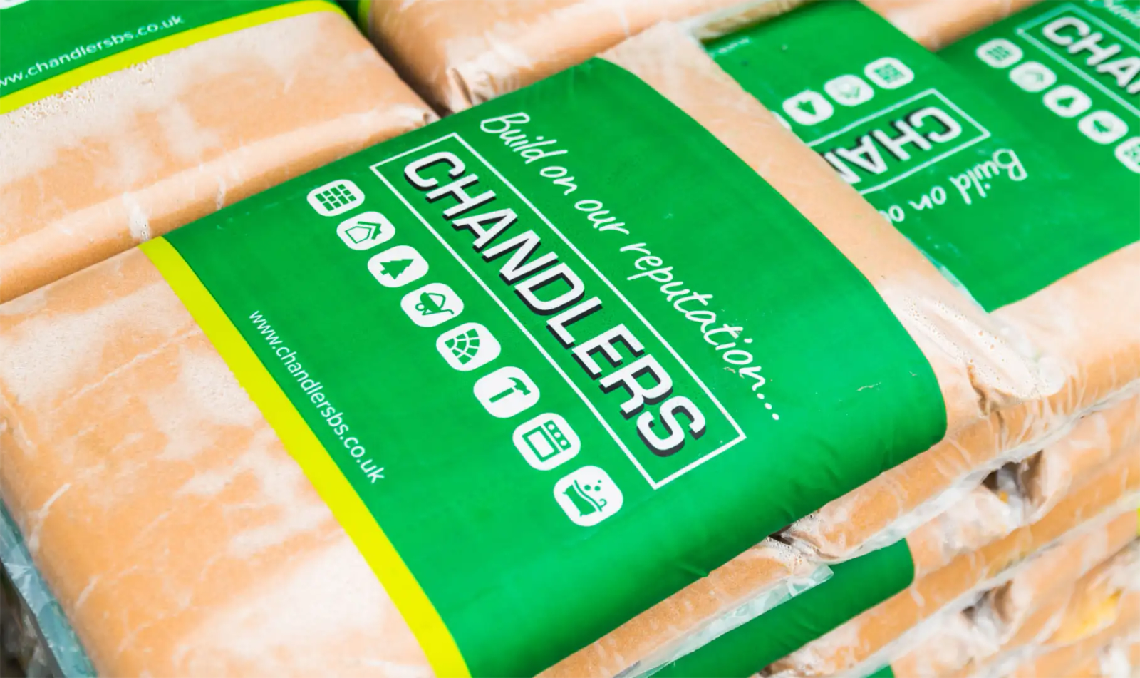 Stacked bags of cement wrapped with a green Chandlers branded band printed with category icons