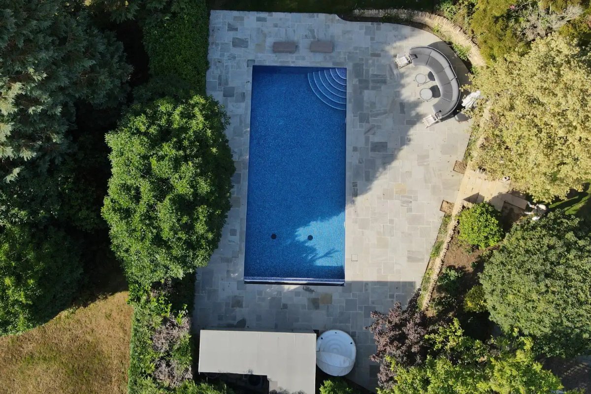 Drone view of a rectangular swimming pool with stone patio surround and curved hot tub seating area