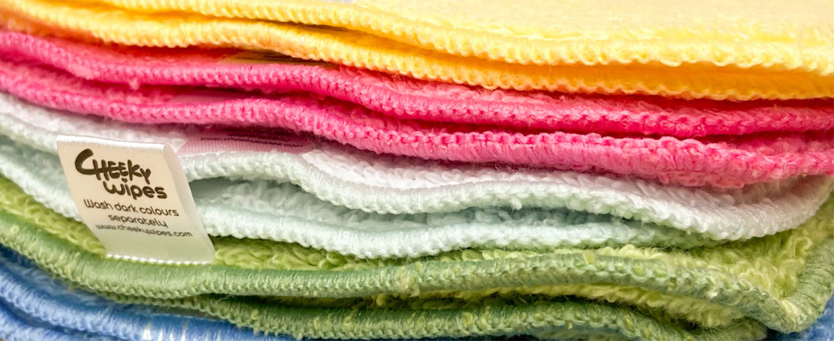 A stack of colourful Cheeky Wipes reusable cloths with a woven label reading 'Cheeky Wipes, wash dark colours separately'