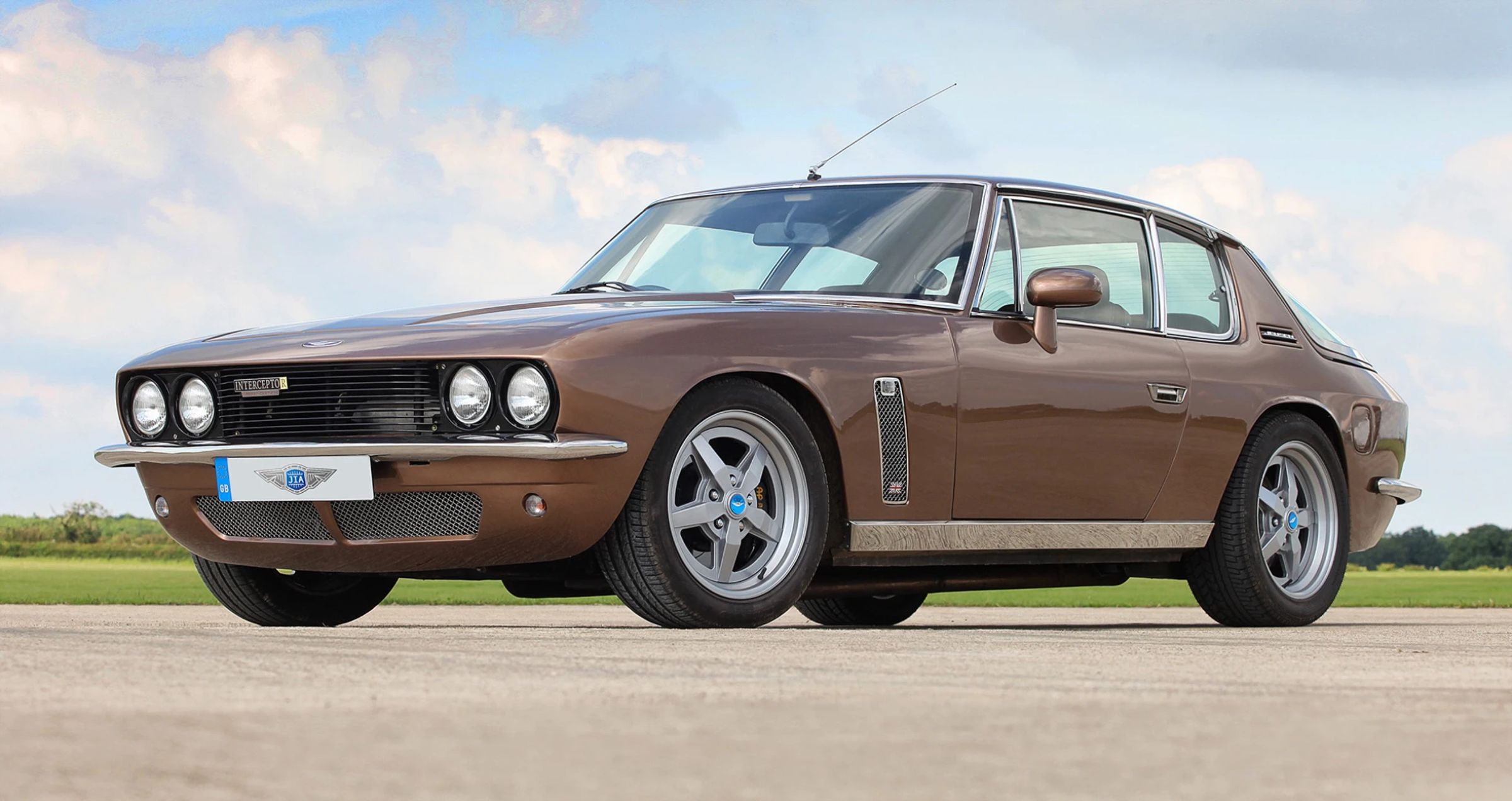 A brown Jensen Interceptor R parked on a runway, viewed from the front three-quarter angle