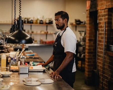 Dishan at the pass of an open kitchen, plates lined up on the counter