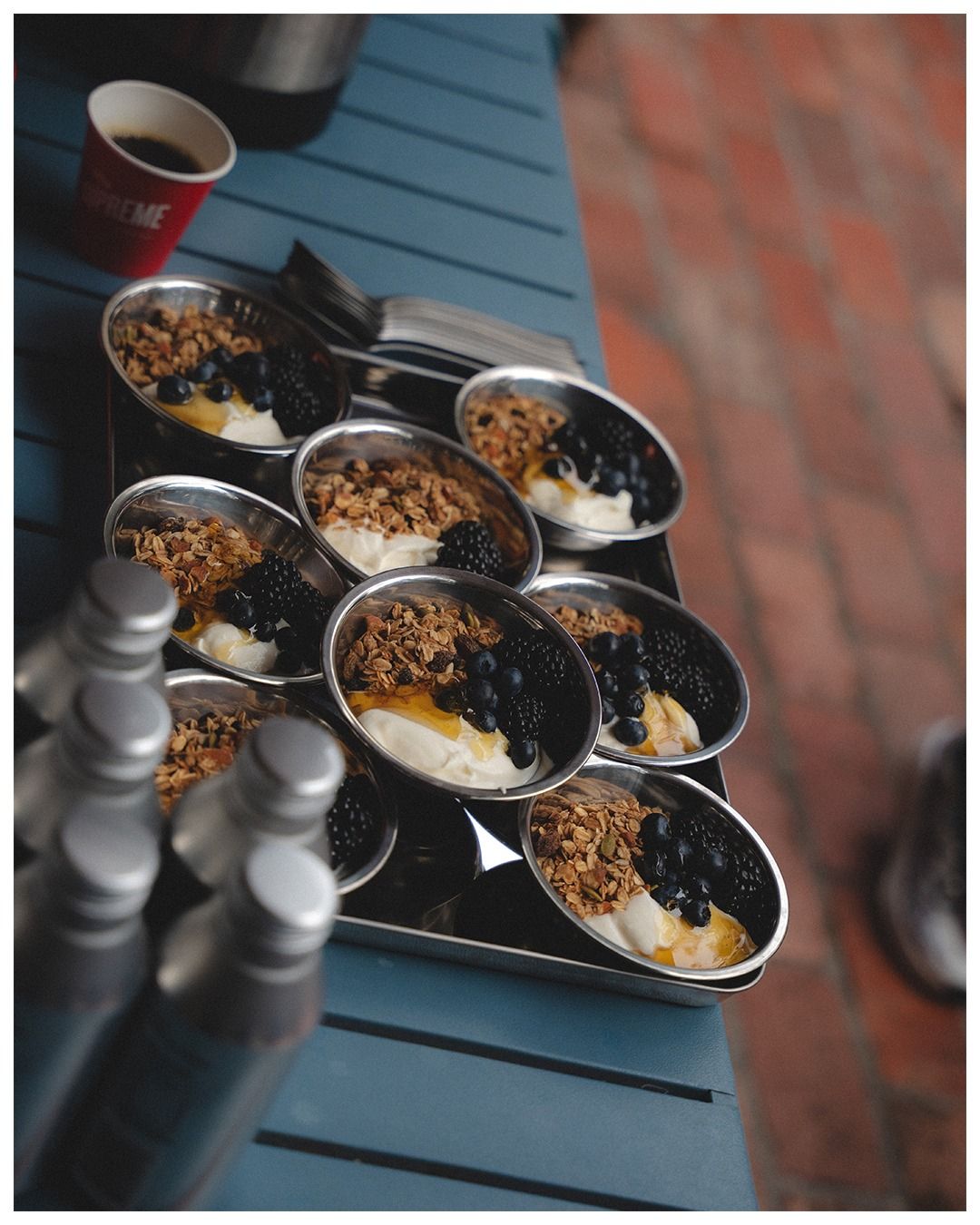 Steel bowls of yoghurt, granola and dark berries on a blue table
