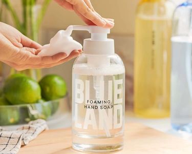 Hand pumps foaming hand soap from Forever bottle on kitchen surface with limes and surface cleaners in background