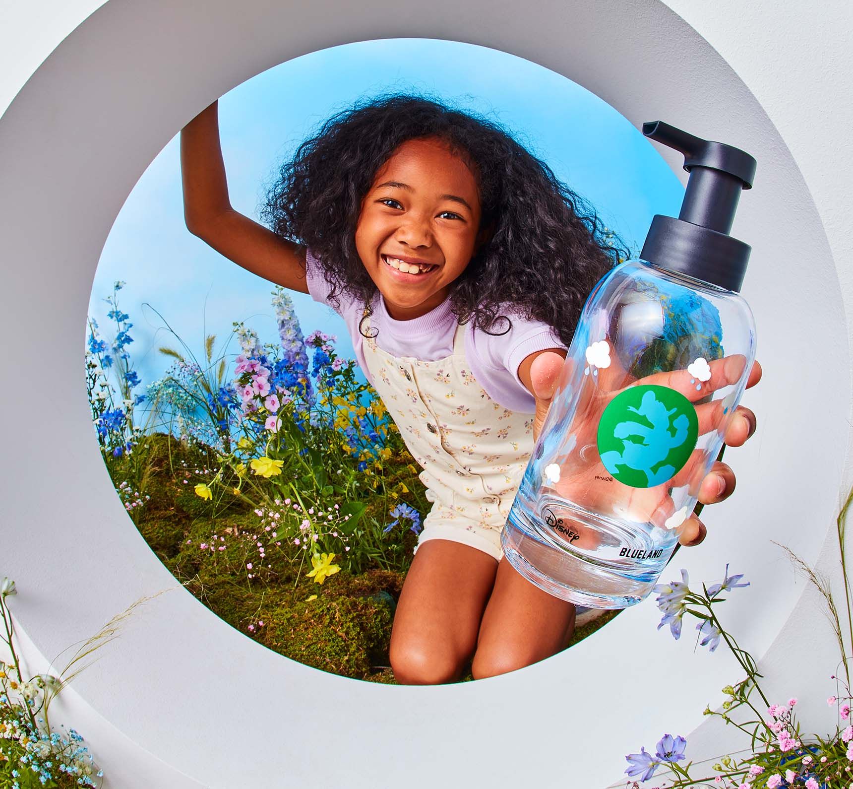 Girl holds blue hand soap bottle featuring Donald Duck on it with flowers in her background.