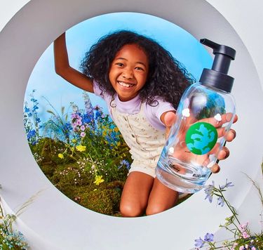 Girl holds blue hand soap bottle featuring Donald Duck on it with flowers in her background.