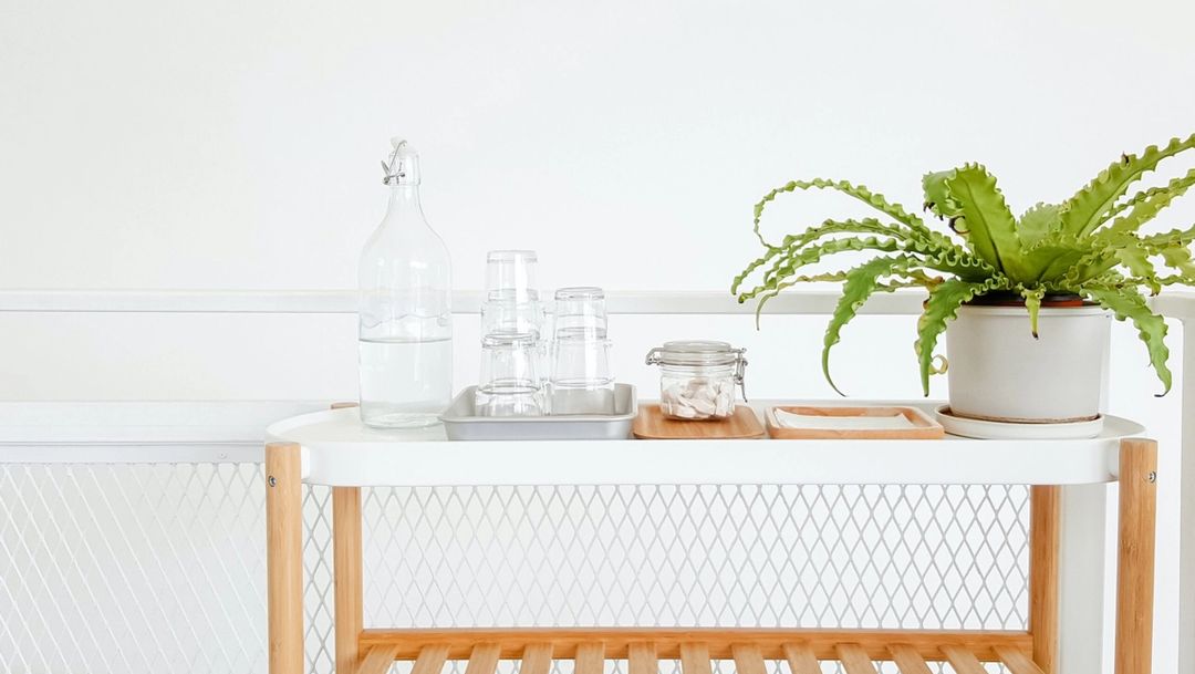 White tray table with green plant, glass water bottle and glass cups
