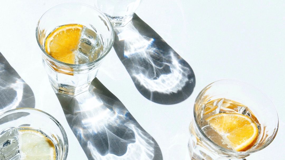 Four water glasses on white table with lemon slices