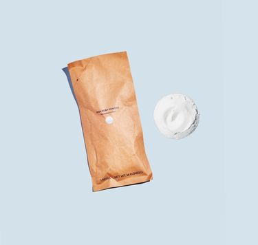 Dish Soap Refill Pouch next to pile of Dish Soap powder against pale blue background