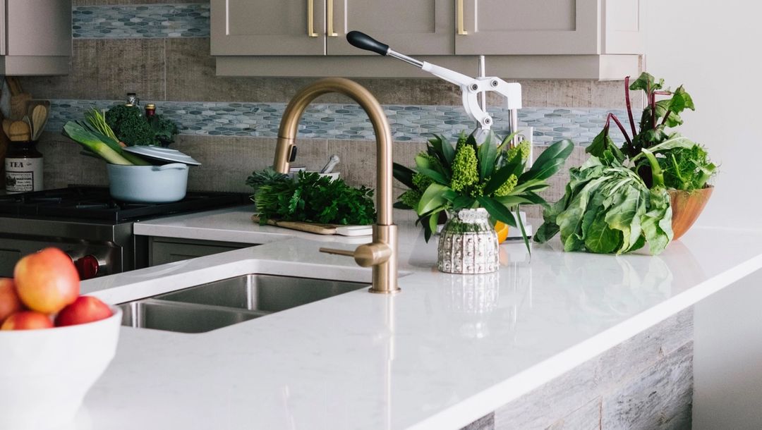 White kitchen countertop with greens and fruit bowl and brass faucet