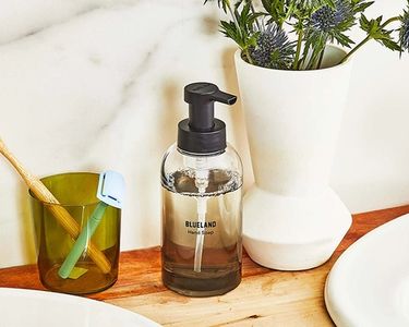 Natural Collection foaming hand soap in slate color by the sink on wooden surface next to white vase