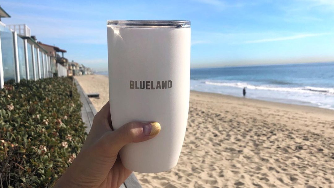 Blueland reusable coffee mug in hand in front of a beach