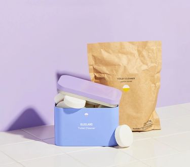 Toilet bowl cleaner starter set: refillable tablet tin with tablets sticking out on white tile and purple background and compostable refill pouch