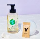 Disney & Blueland bottle with Daisy Duck logo on white tile next to table in compostable wrapper and 2 naked tablets on bubble with purple background