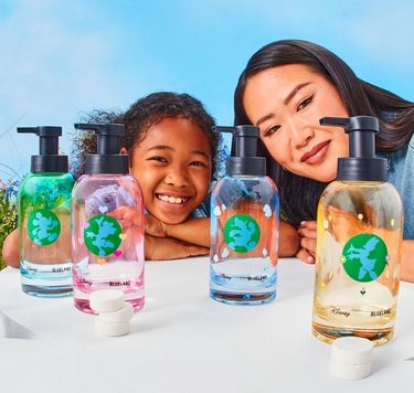 Young girl and mother posed behind Disney & Blueland hand soap bottles on surface with hand soap refills on table
