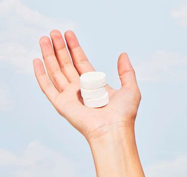 Hand holding 3 unwrapped Blueland Foaming Hand Soap tablets against blue sky