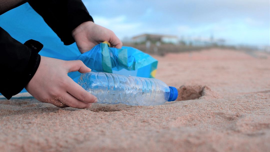 hand cleaning up single-use plastic bottle off of beach