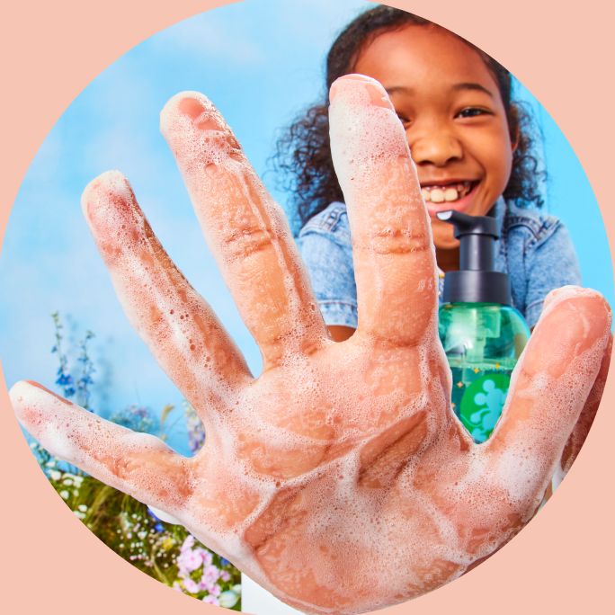 Young girl holds hand of foaming hand soap up close with bottle of soap next to her